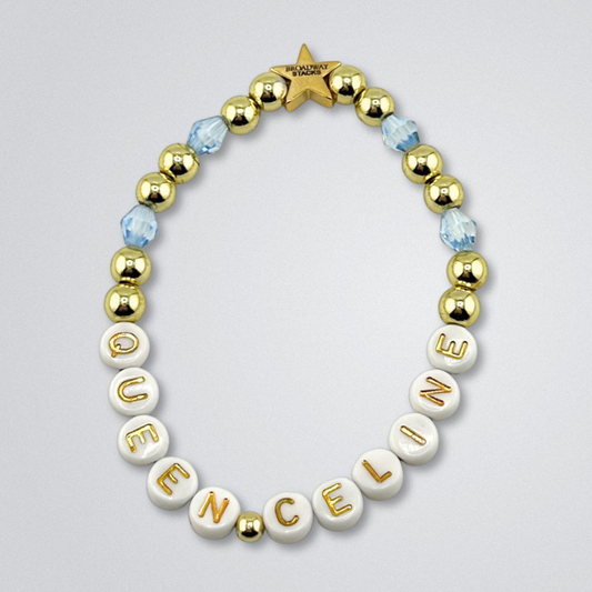 Bead bracelet with letter beads spelling 'QUEEN CELINE' on a gray background. Broadway Stacks UNSINKABLE Collection. Blue and gold colored beads. Gold star logo bead to remind you that you shine. Inspired by Titanique the Musical.