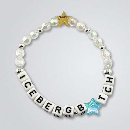 Bead bracelet with letter beads spelling 'ICEBERG B*TCH' on a gray background. Broadway Stacks UNSINKABLE Collection. Clear, white and silver colored beads. A blue star bead for the letter I. Gold star logo bead to remind you that you shine. Inspired by Titanique the Musical.