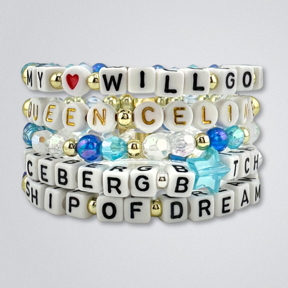 Stacked bead bracelets with letter beads on a gray background, part of the Broadway Stacks UNSINKABLE Collection. Blues, white, clear and gold colored beads. Gold star logo bead to remind you that you shine. Inspired by Titanique the Musical.