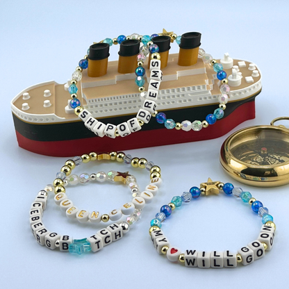 Bead bracelets with letter beads in front of a Titanic model ship on a light blue background. Part of the Broadway Stacks UNSINKABLE Collection. Inspired by Titanique the Musical.