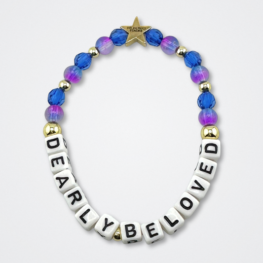 Broadway Stacks CAKE Collection. Dearly Beloved bracelet with blue, purple and gold colored beads. Letter beads that spell quote. Star logo bead to remind you that you shine. Two Strangers Carry a Cake Across New York fans.