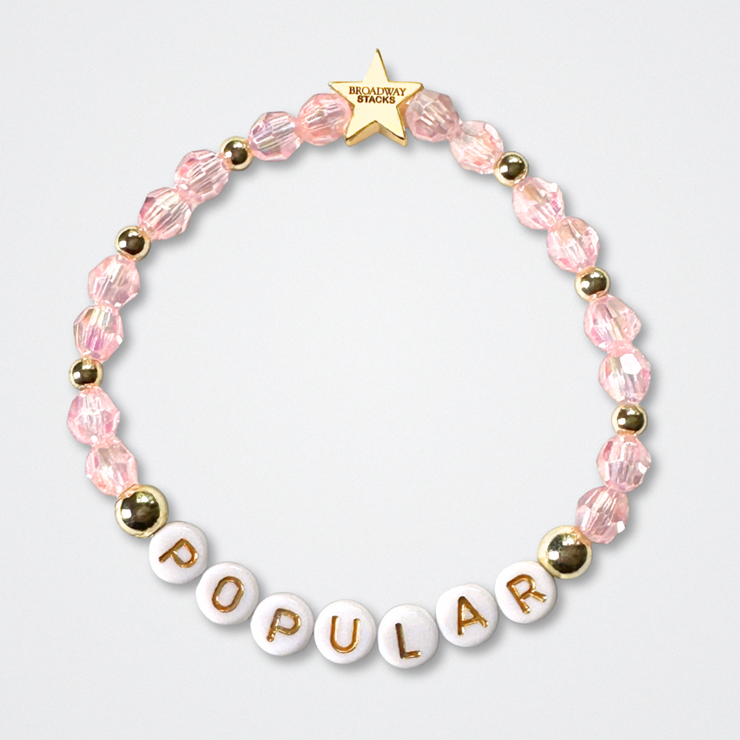 Beaded bracelet with 'POPULAR' letters on a light gray background. Broadway Stacks WITCH collection. Pink and gold colored beads. Gold star logo bead to remind you that You Shine. 