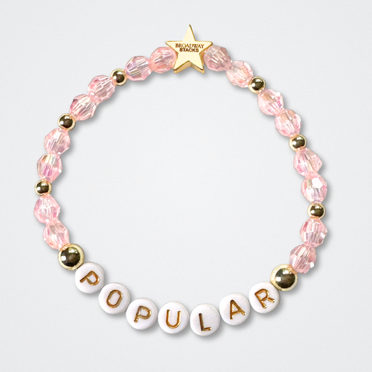 Beaded bracelet with 'POPULAR' letters on a light gray background. Broadway Stacks WITCH collection. Pink and gold colored beads. Gold star logo bead to remind you that You Shine. 