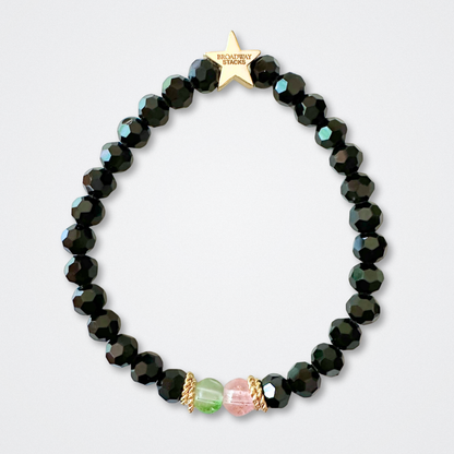 Black bead bracelet with one green and one pink bead in the middle on a light gray background. Broadway Stacks WITCH collection. Gold star logo bead to remind you that You Shine. 