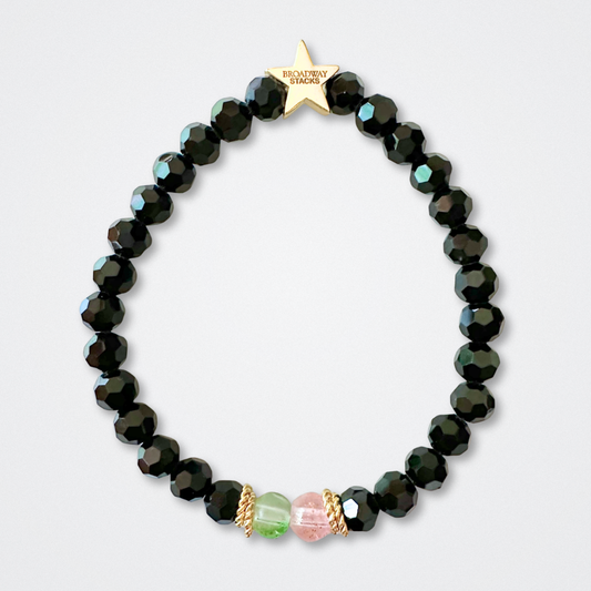 Black bead bracelet with one green and one pink bead in the middle on a light gray background. Broadway Stacks WITCH collection. Gold star logo bead to remind you that You Shine. 