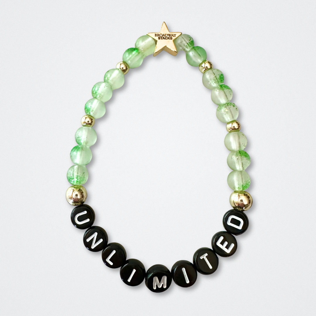 Beaded bracelet with 'UNLIMITED' letters on a light gray background. Broadway Stacks WITCH collection. Green and gold colored beads. Gold star logo bead to remind you that You Shine. 