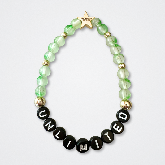 Beaded bracelet with 'UNLIMITED' letters on a light gray background. Broadway Stacks WITCH collection. Green and gold colored beads. Gold star logo bead to remind you that You Shine. 
