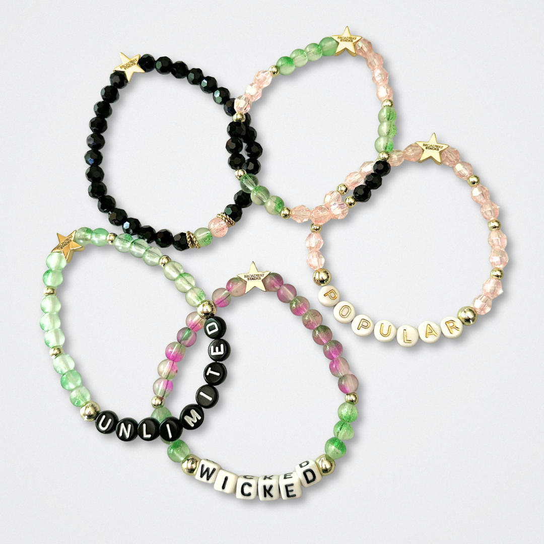 Set of beaded bracelets with word beads on a light gray background. Broadway Stacks WITCH collection. Greens, pinks, black and gold colored beads. Gold star logo bead to remind you that You Shine. 