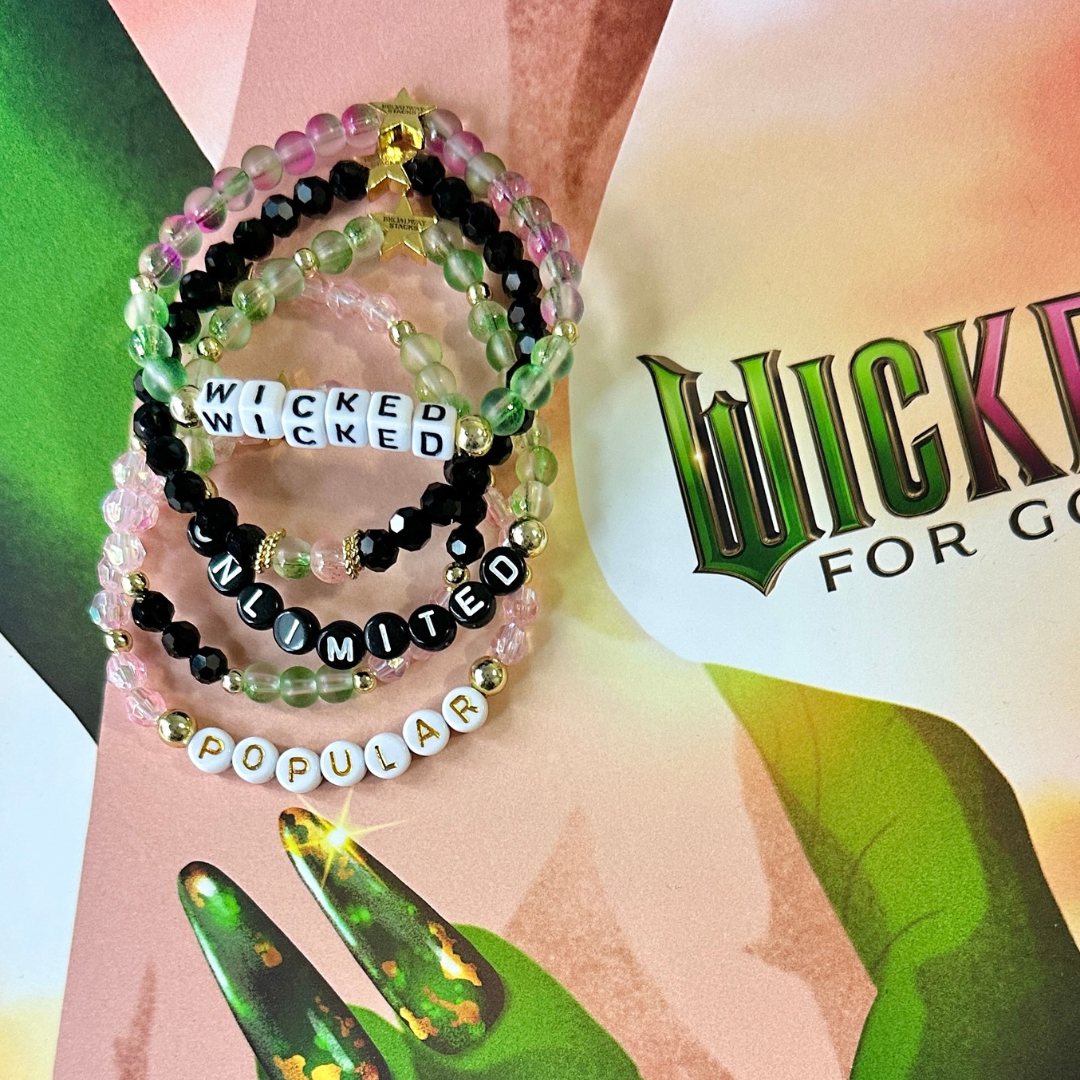 Beaded bracelet stack on a Wicked For Good background. Broadway Stacks WITCH collection. Greens, pinks, black and gold colored beads. Gold star logo bead to remind you that You Shine. 