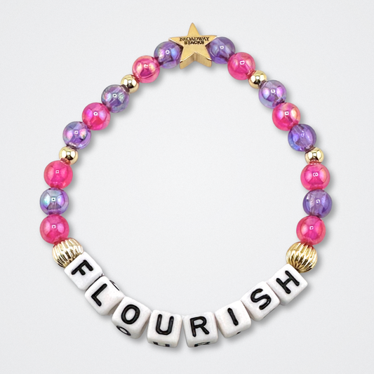 Broadway Stacks GARDEN bracelet with pink, purple and gold color beads. Letters say FLOURISH. Displayed on a gray background.