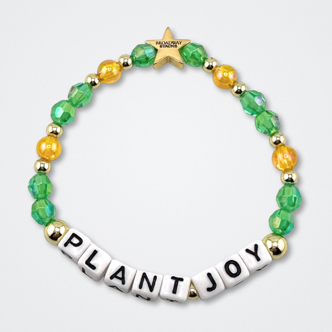 Broadway Stacks GARDEN bracelet with green, yellow and gold color beads. Letters say PLANT JOY. Displayed on a gray background.