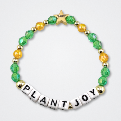 Broadway Stacks GARDEN bracelet with green, yellow and gold color beads. Letters say PLANT JOY. Displayed on a gray background.