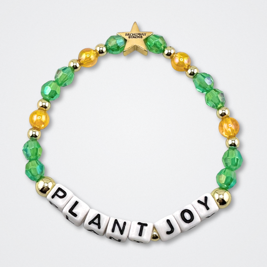Broadway Stacks GARDEN bracelet with green, yellow and gold color beads. Letters say PLANT JOY. Displayed on a gray background.