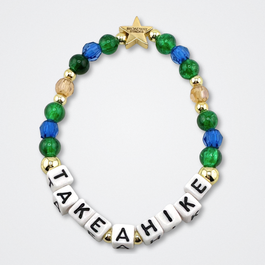 Broadway Stacks TAKE A HIKE bead bracelet. Green, blue, tan and gold color beads on a gray background.