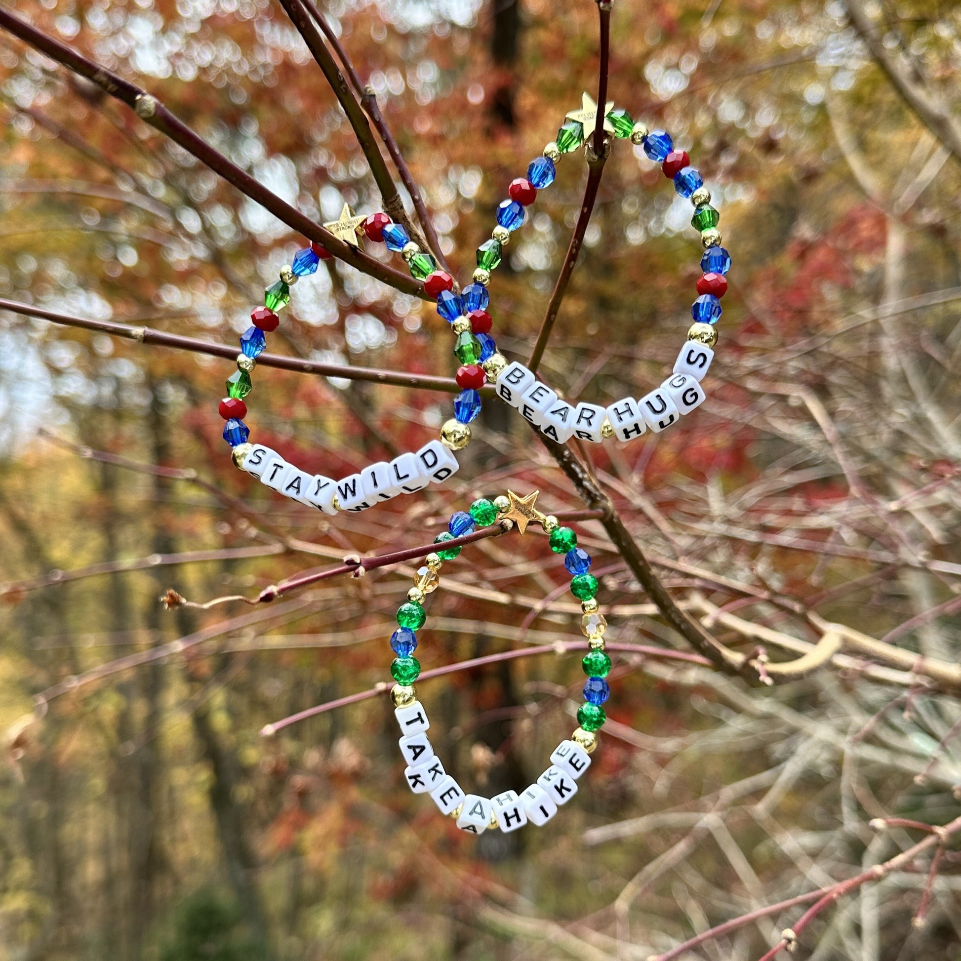 Broadway Stacks MOUNTAIN Collection bead bracelets. Green, blue, dark red and gold color jewelry displayed on tree limbs in the mountains.