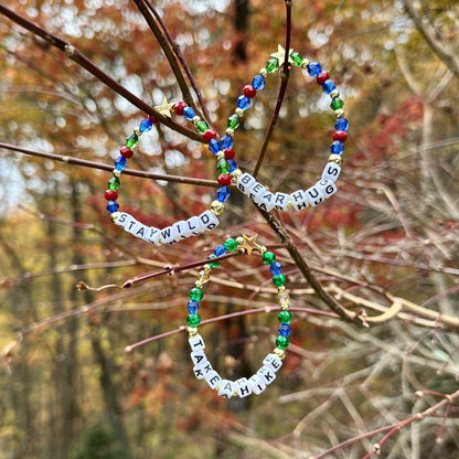 Broadway Stacks MOUNTAIN Collection bead bracelets. Green, blue, dark red and gold color jewelry displayed on tree limbs in the mountains.