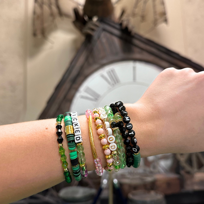 Broadway Stacks Witch collection. 3 stretch bracelets included in Stack. Greens, pinks, black and gold colored beads. Letter beads that spell Wicked. Gold star logo bead on every bracelet. 