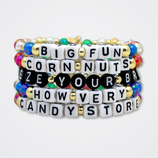 Broadway Stacks CORN NUTS Collection. 5 stretch bracelets included in Stack. Red, yellow, green, blue, black and gold colored beads. Letter beads that spell quotes. Gold star logo bead to remind you that you shine. Heathers the Musical fans.