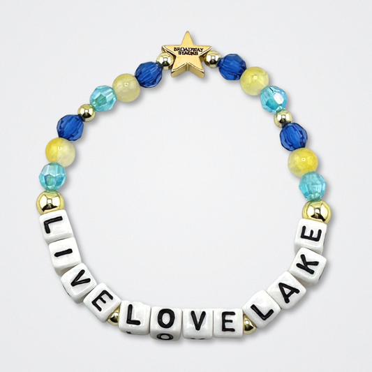 Broadway Stacks LIVE LOVE LAKE bead bracelet. Blues, yellow and gold color beads on a gray background.