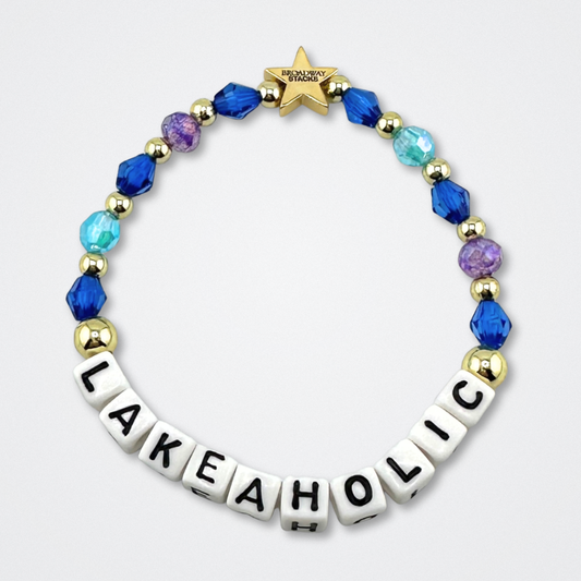 Broadway Stacks LAKEAHOLIC bead bracelet. Blues, purple and gold color beads on a gray background.