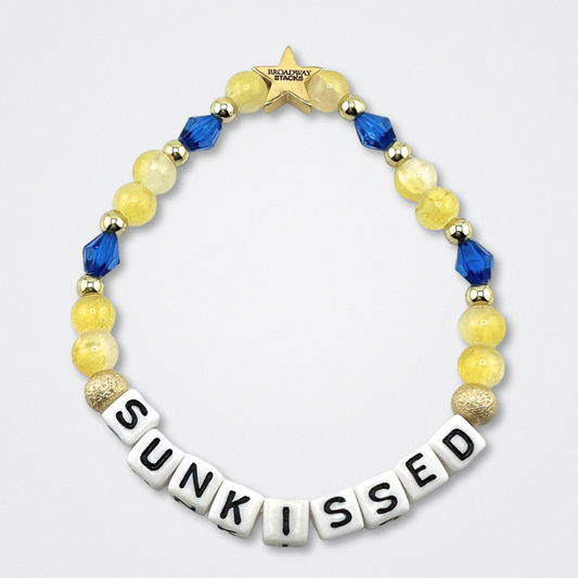 Broadway Stacks SUNKISSED bead bracelet. Yellow, blue and gold color beads on a gray background.