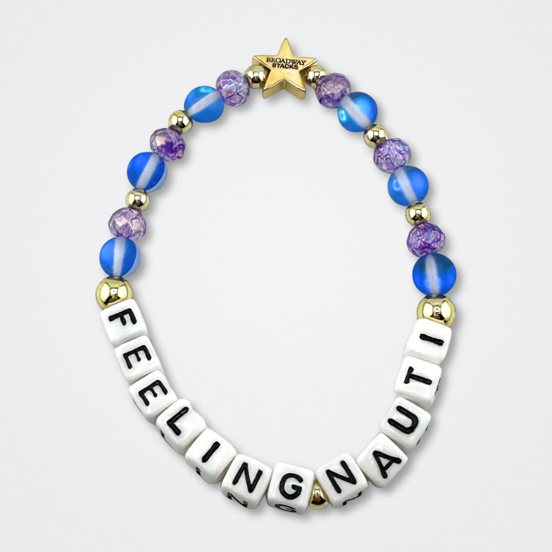 Broadway Stacks FEELING NAUTI bead bracelet. Purple, blue and gold color beads on a gray background.