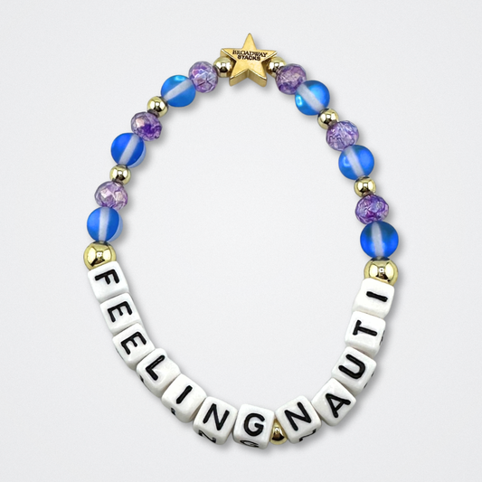 Broadway Stacks FEELING NAUTI bead bracelet. Purple, blue and gold color beads on a gray background.