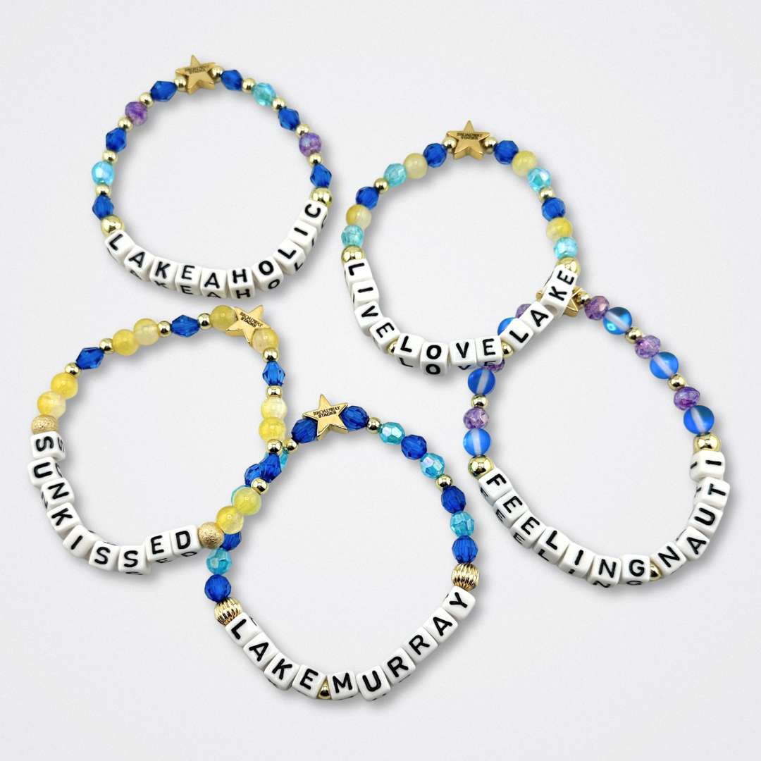 Broadway Stacks LAKE LIFE bracelet collection. Blues, yellow, purple and gold color bead bracelets laying flat on gray background.