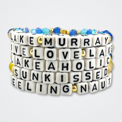 Broadway Stacks LAKE LIFE bracelet collection. Blues, yellow, purple and gold color bead bracelets stacked on gray background.