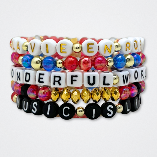 Broadway Stacks JAZZY Collection. 5 stretch bracelets included in Stack. Red, blue, black and gold colored beads. Letter beads that spell quotes. Gold star logo bead to remind you that you shine. Wonderful World musical and Louis Armstrong fans.