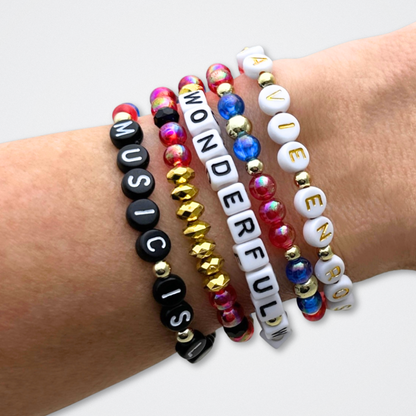 Broadway Stacks JAZZY Collection. 5 stretch bracelets included in Stack. Red, blue, black and gold colored beads. Letter beads that spell quotes. Gold star logo bead to remind you that you shine. Wonderful World musical and Louis Armstrong fans.